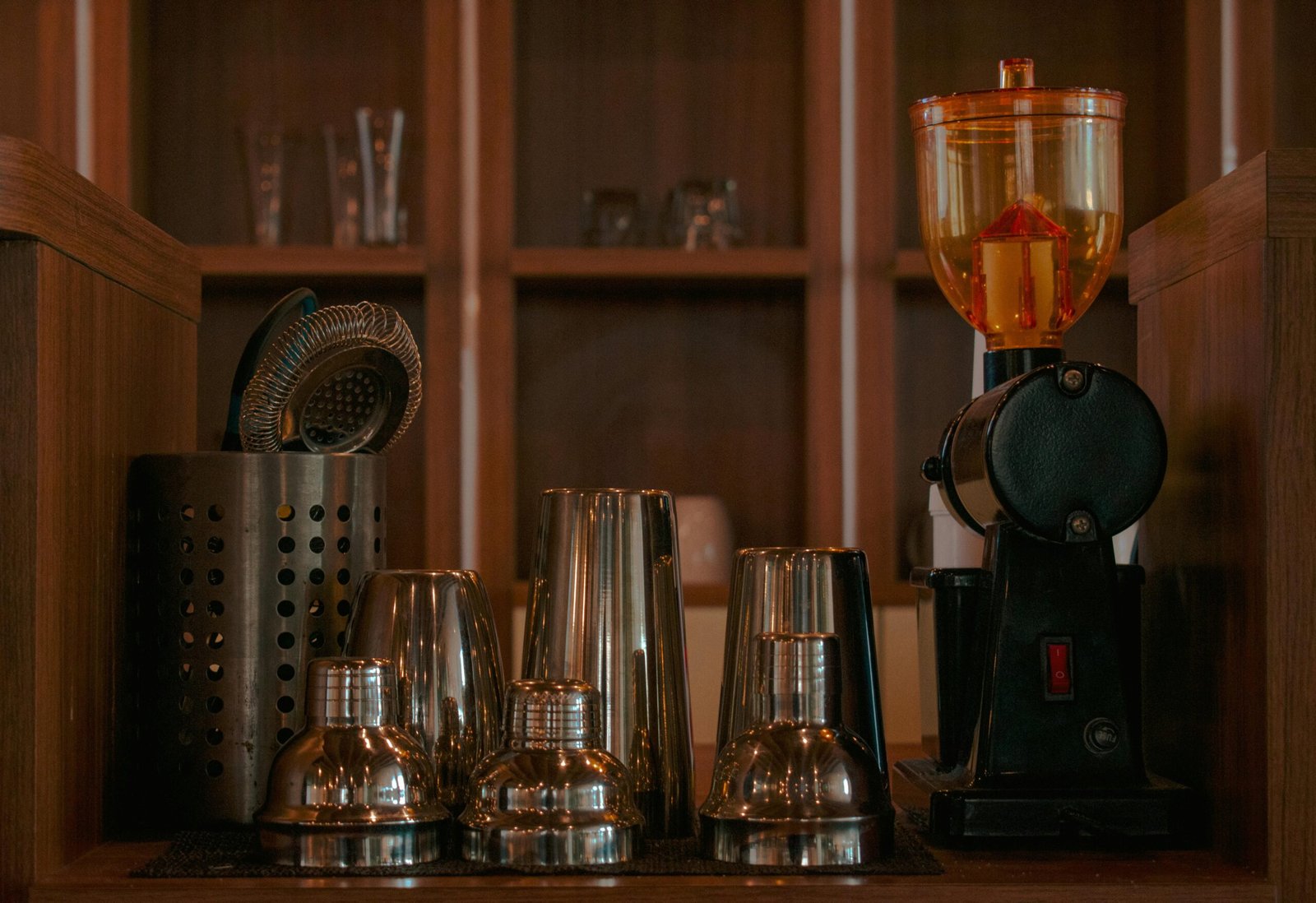 Organized bar equipment including shakers and a coffee grinder on wooden shelves.