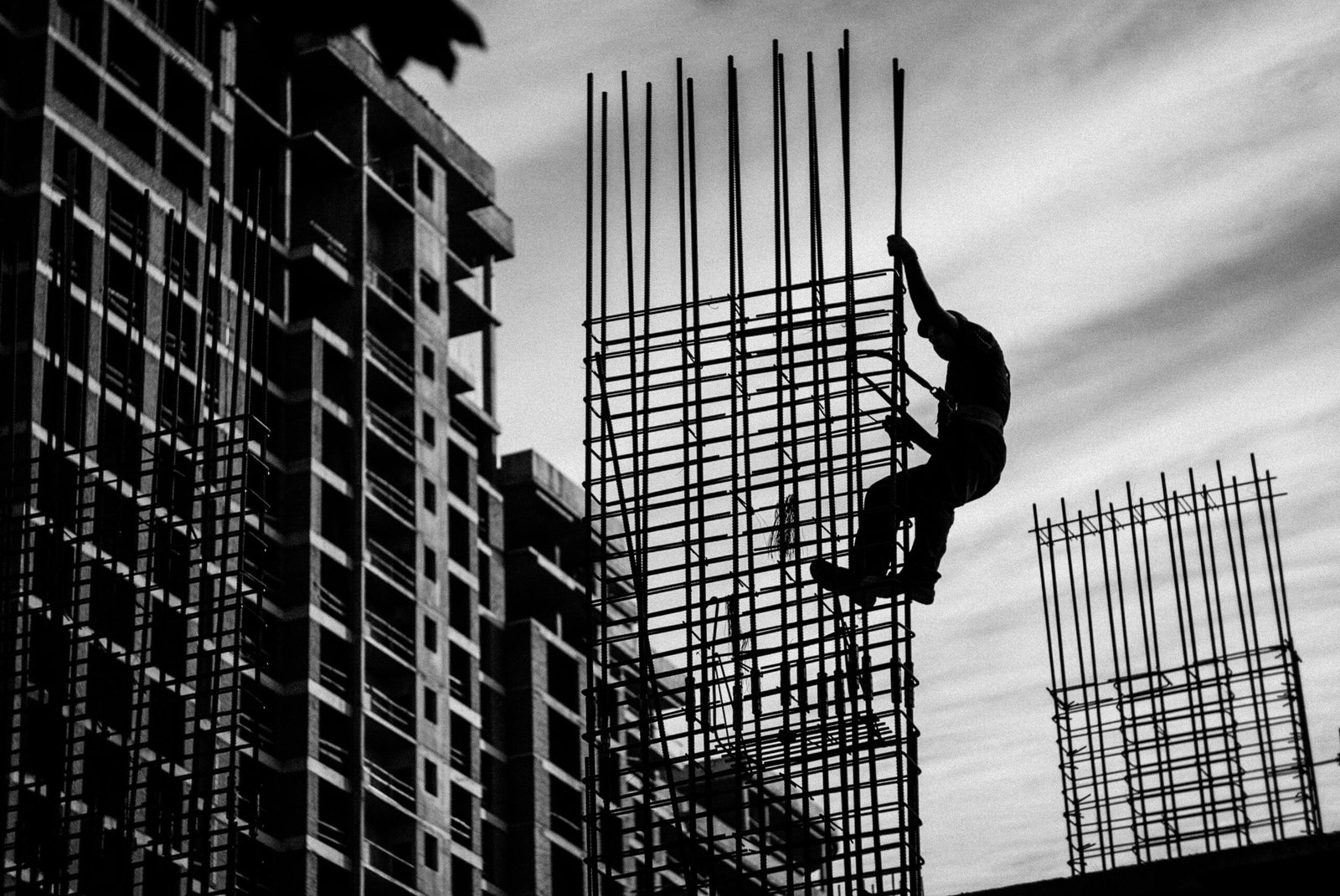 Black and white silhouette of a construction worker climbing steel rods on a building site.