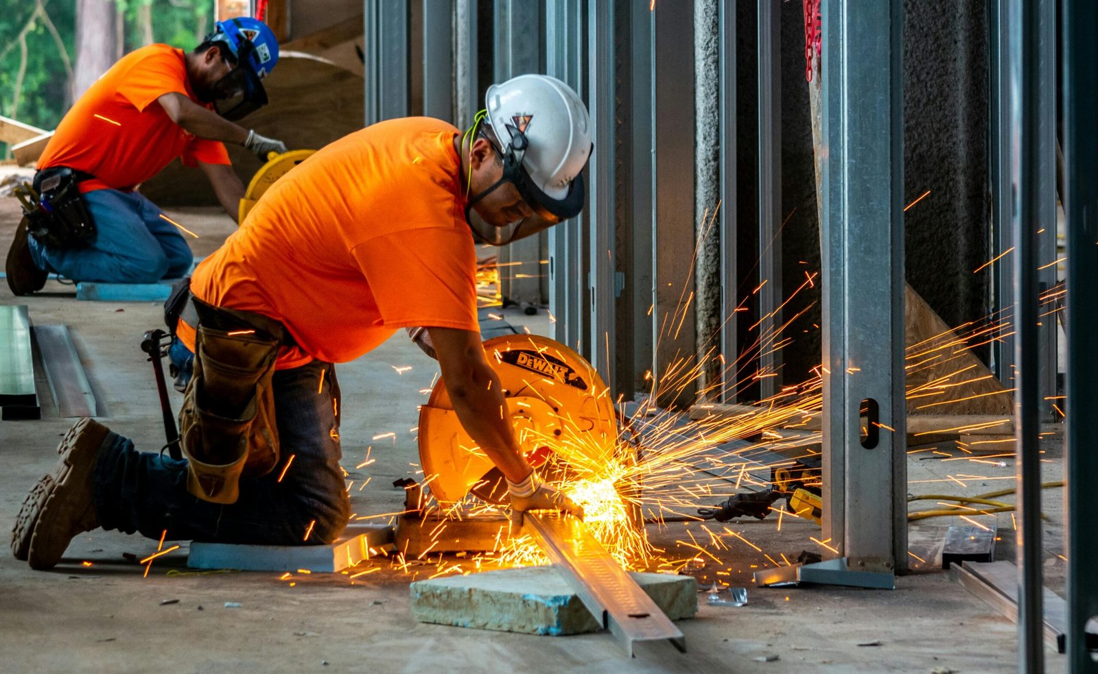 Workers cutting metal beams with a grinder, creating sparks inside a construction site.